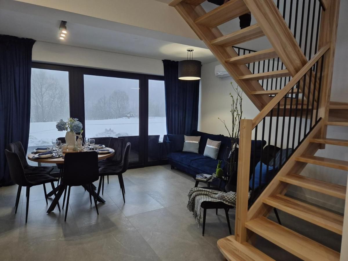 Salon z jadalnią, granatową kanapą i drewnianymi schodami na piętro